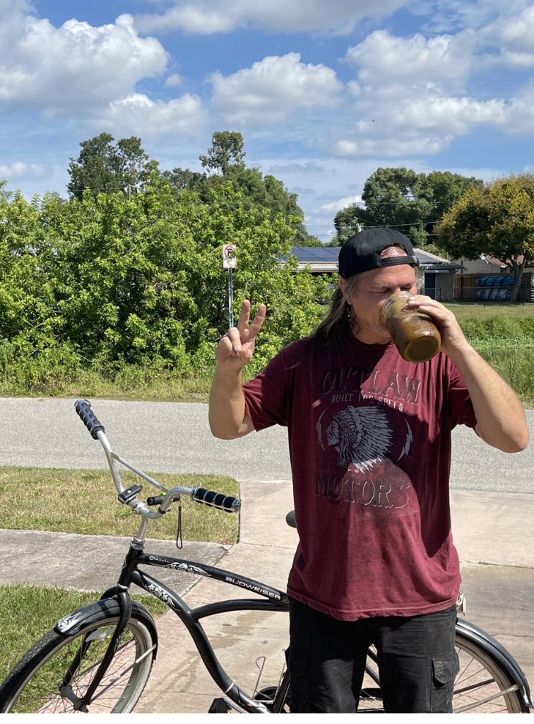 Greg drinking EcoFit from a mason jar, throwing a peace sign by his bike